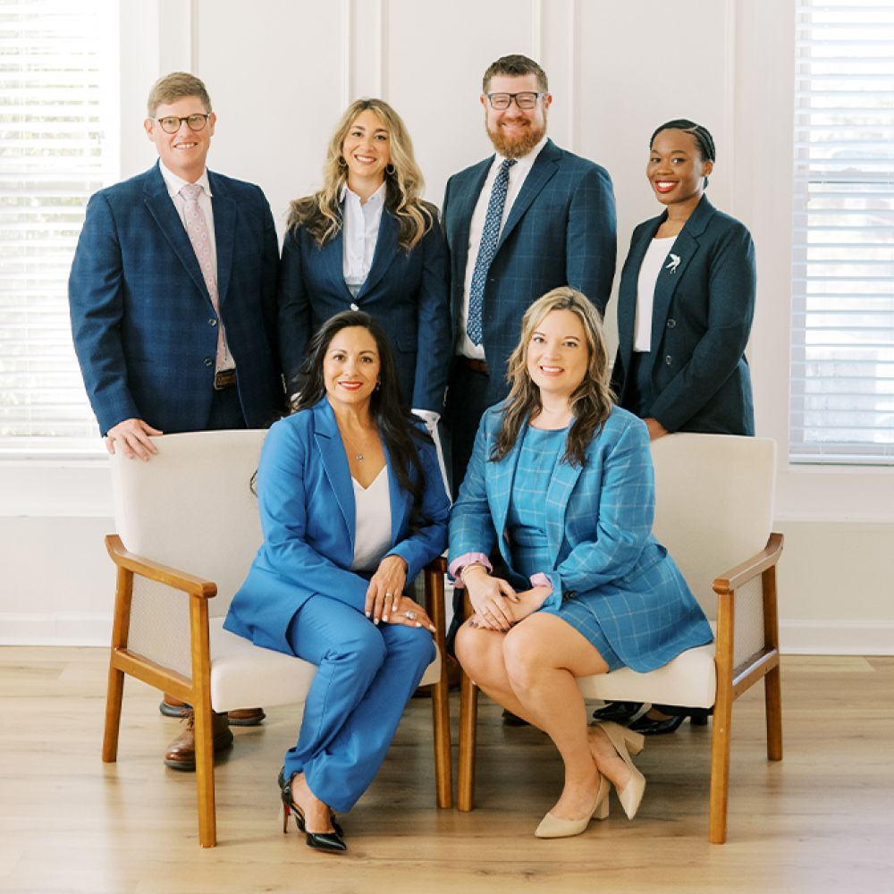 A diverse team in business attire, smiling and posing confidently in a bright office setting.