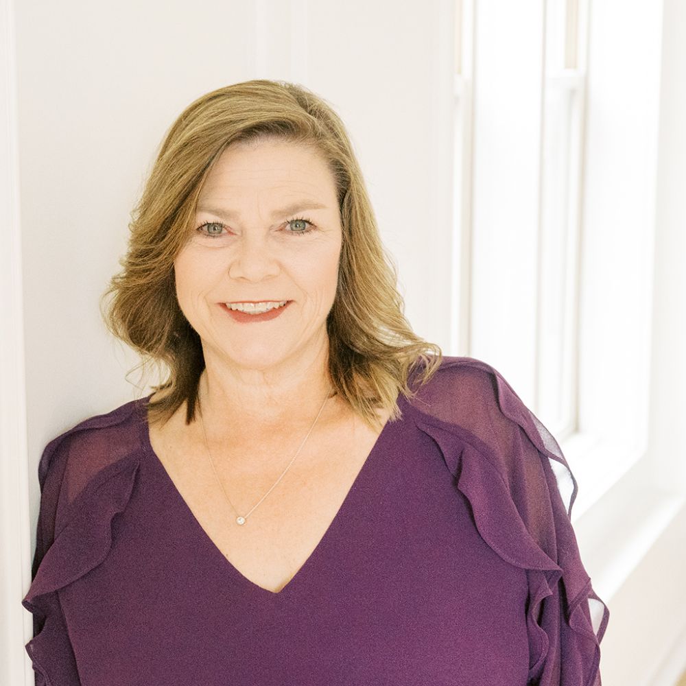 Wendy Phifer in a purple dress smiling in a bright, naturally lit room.