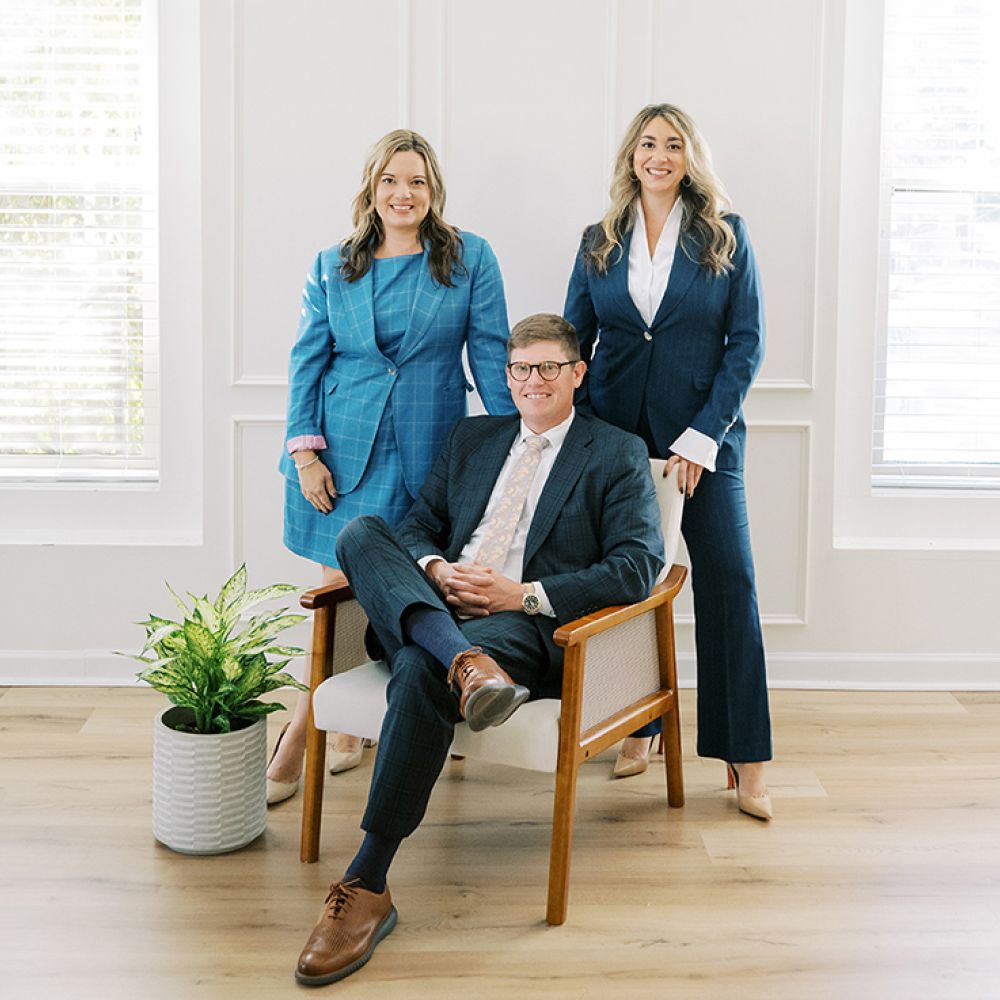 Tee Leitner, Ellie Bragg, and Jordan Griffin posing in office setting near window and plant.