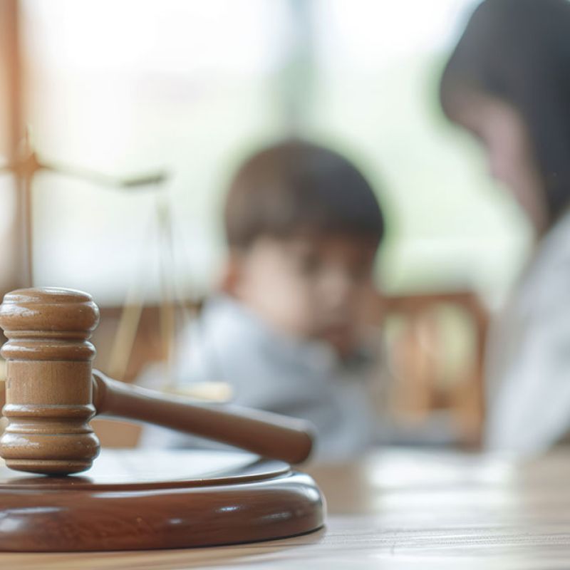 Gavel and scales of justice in focus with blurred child and parent in background, symbolizing family law.