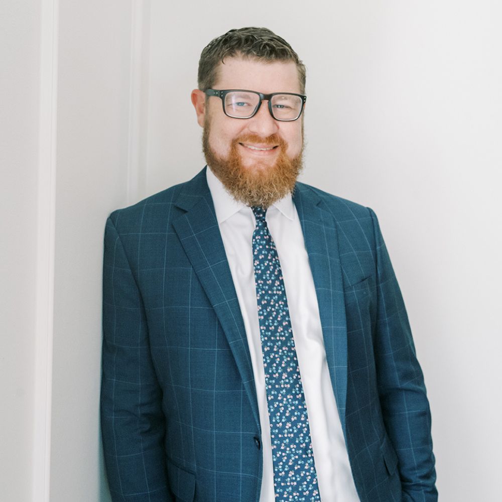 Tim Cannady in a blue suit and patterned tie smiling against a light wall background.