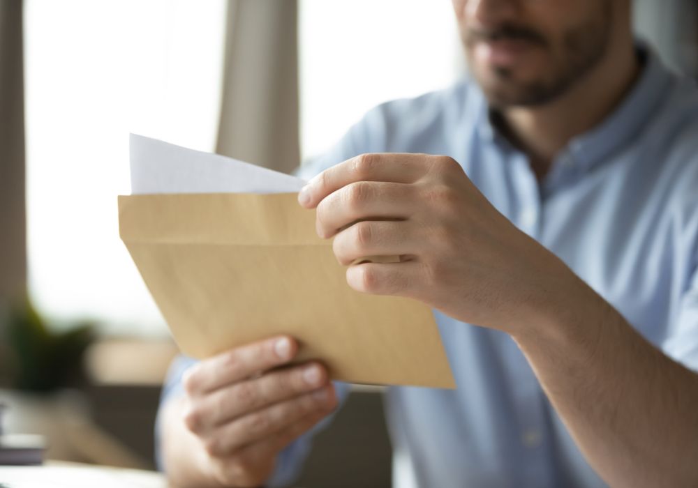 Man opening envelope, revealing letter content, in casual setting.