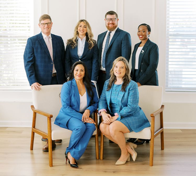 A diverse team in business attire, smiling and posing confidently in a bright office setting.