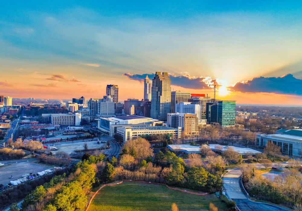 Aerial view of a vibrant city skyline at sunset, featuring modern buildings, roads, and lush green spaces.