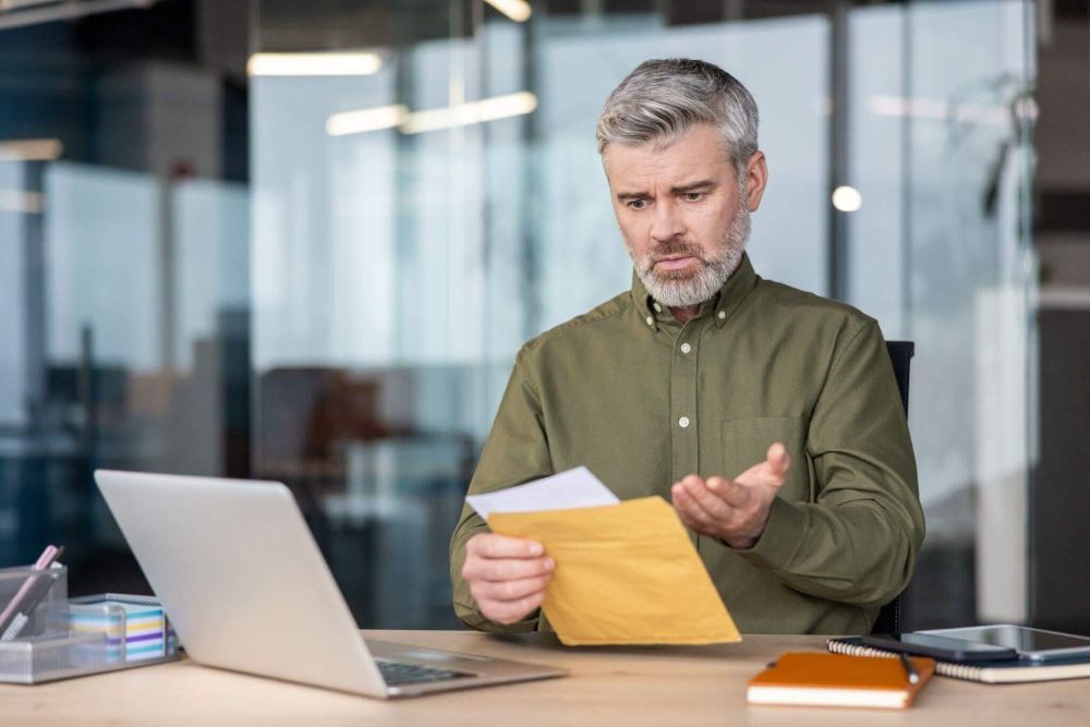 a man holding a piece of paper in front of a laptop