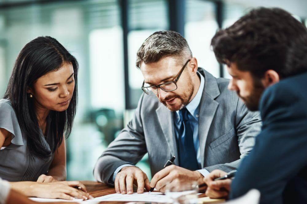 a group of people sitting around a table working on paperwork