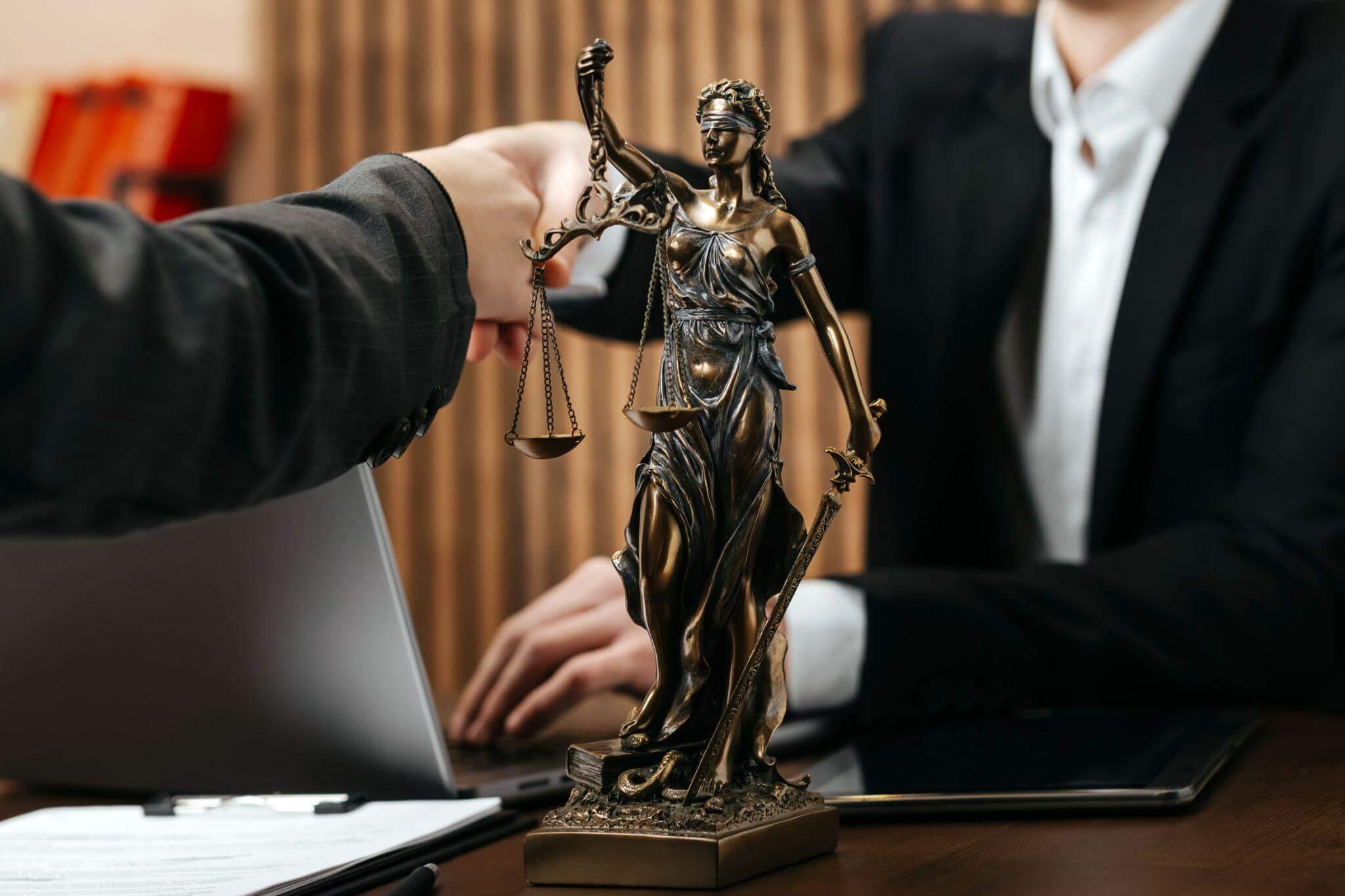 Lady Justice statue receiving a laptop, symbolizing