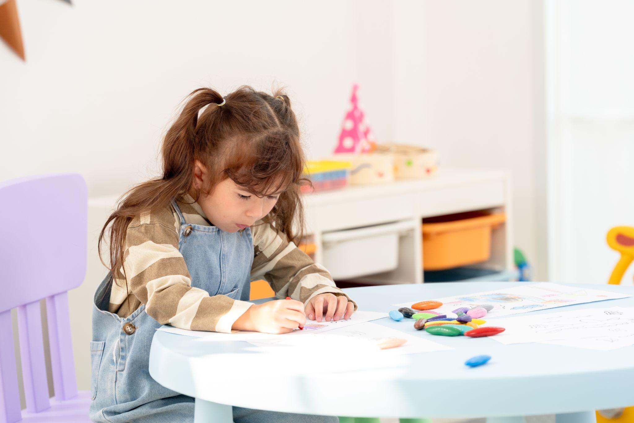 Little girl playing with crayons at a table